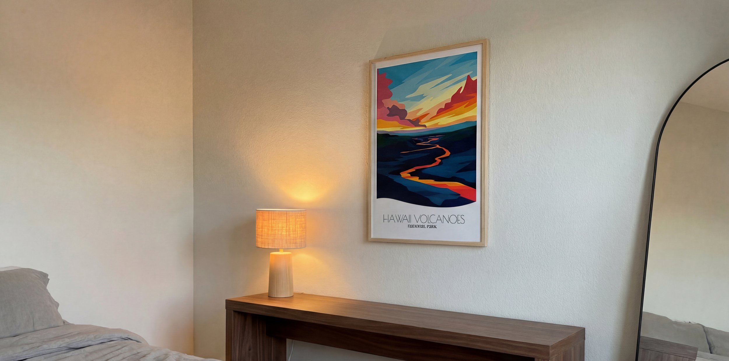 Interior of a bedroom with a framed poster of Hawaii Volcanoes National Park, a table with a lamp, and a mirror.
