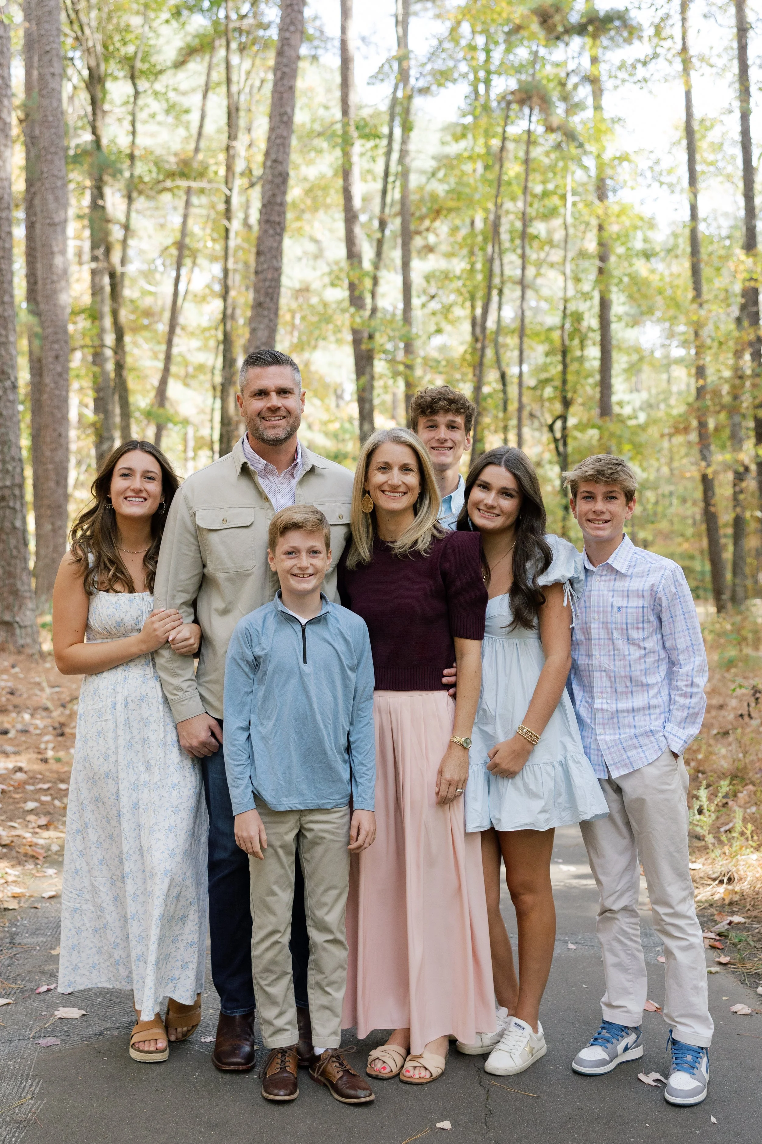 A family of eight posing outdoors on a forest trail during fall.