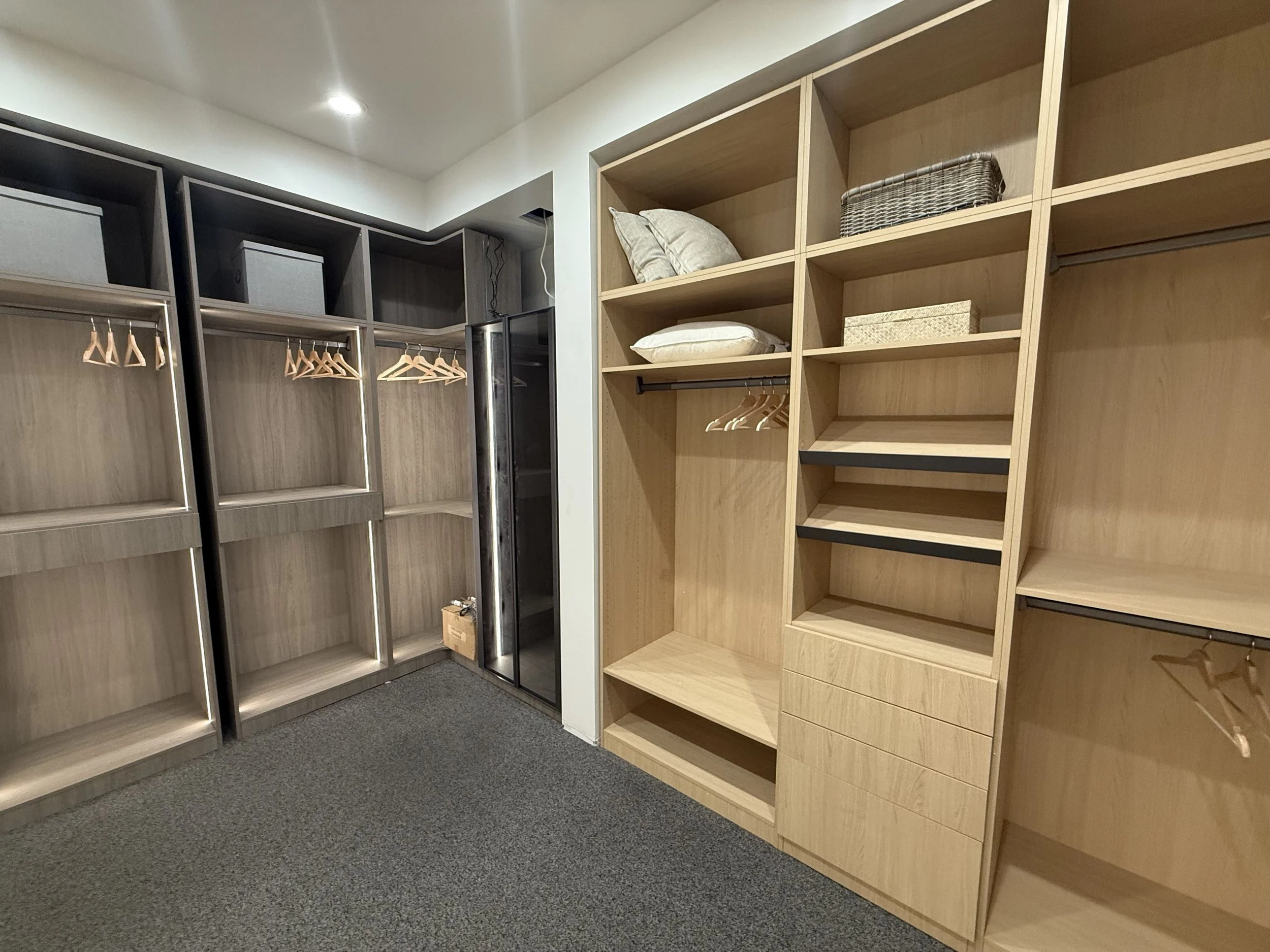 Empty walk-in closet with wooden and metal shelves, hanging rods, pillows, storage boxes, and a small fridge.