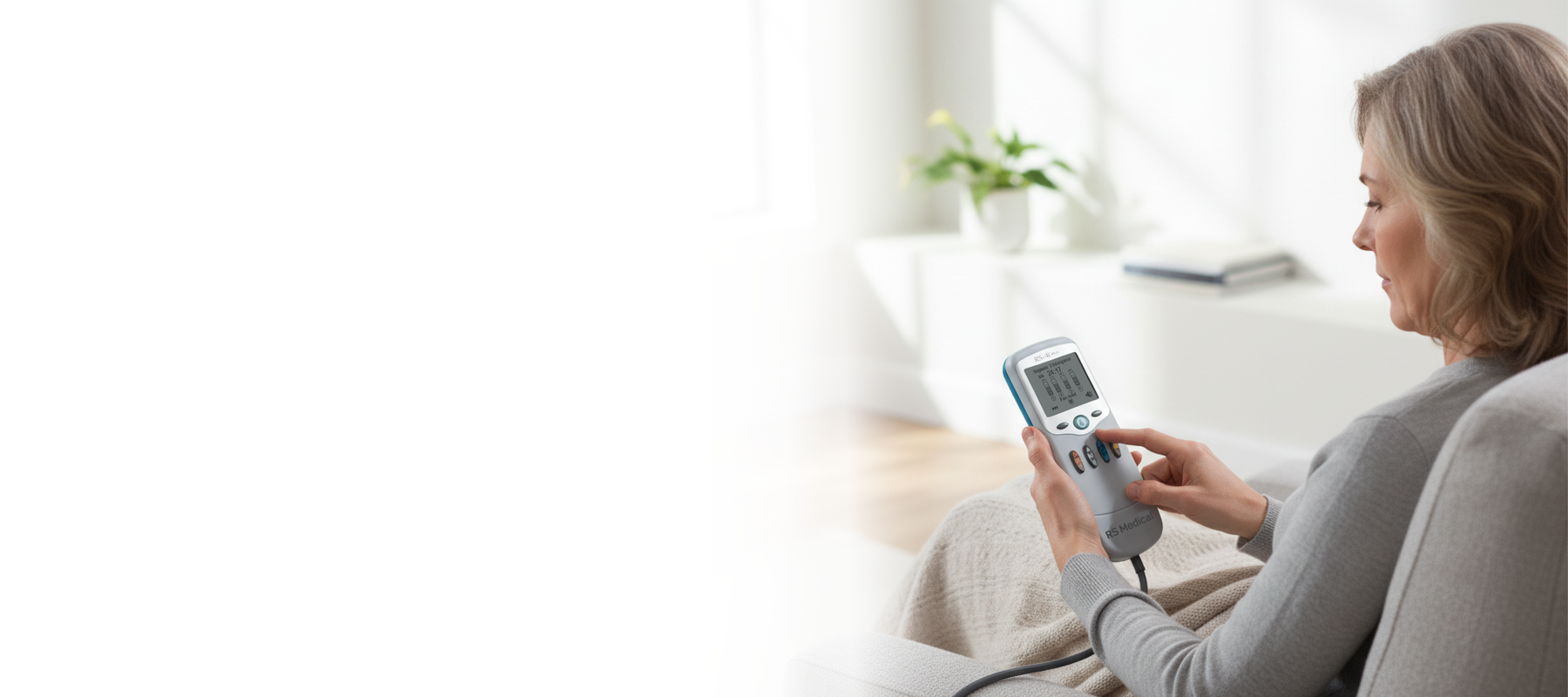 A woman sitting on a light gray armchair, holding RS-4i Plus device while taking a treatment.