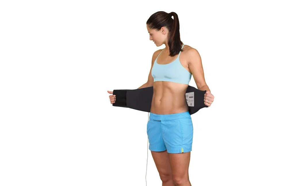 Woman in blue sports bra and shorts putting the RS-LBG Low Back Garment on.