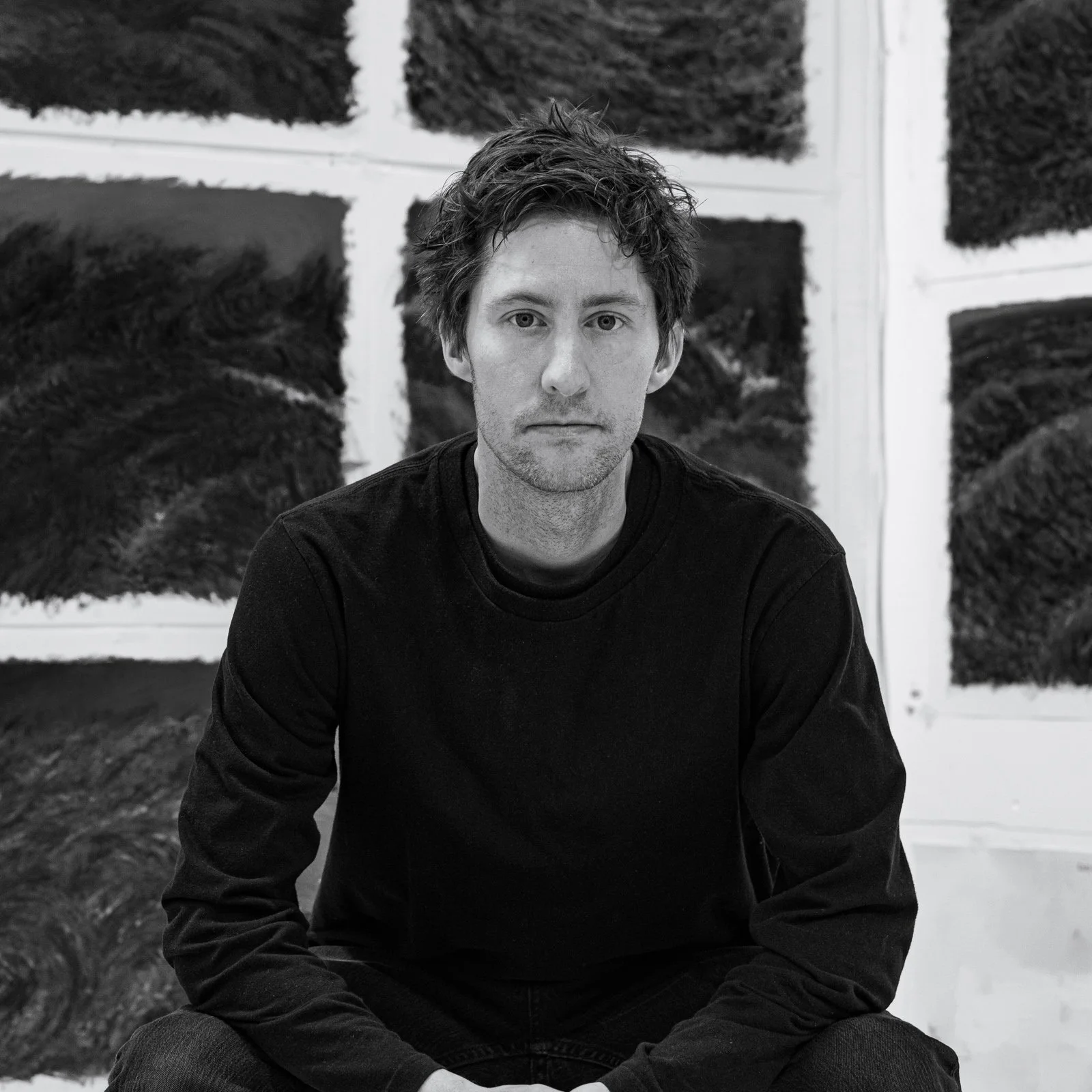 Woman with long brown hair wearing a black turtleneck, looking at camera in front of gray background.