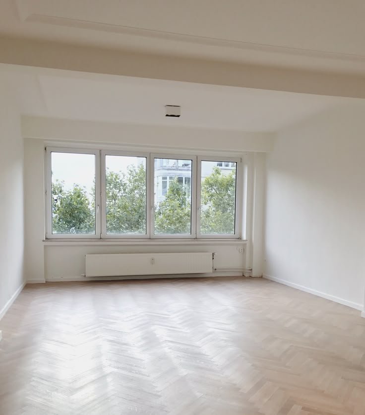 Empty room with large windows and herringbone wood floor