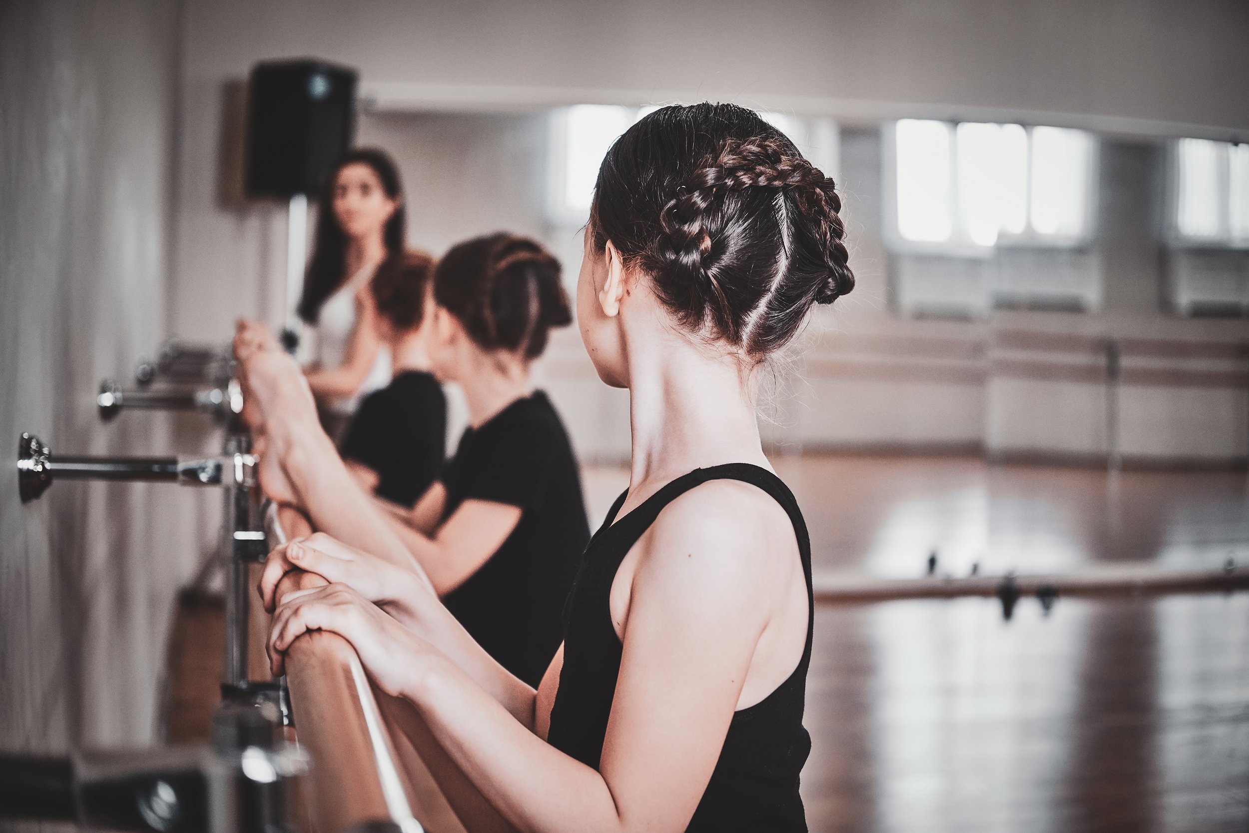 Ballet students practicing at a barre in a dance studio with mirrored walls.