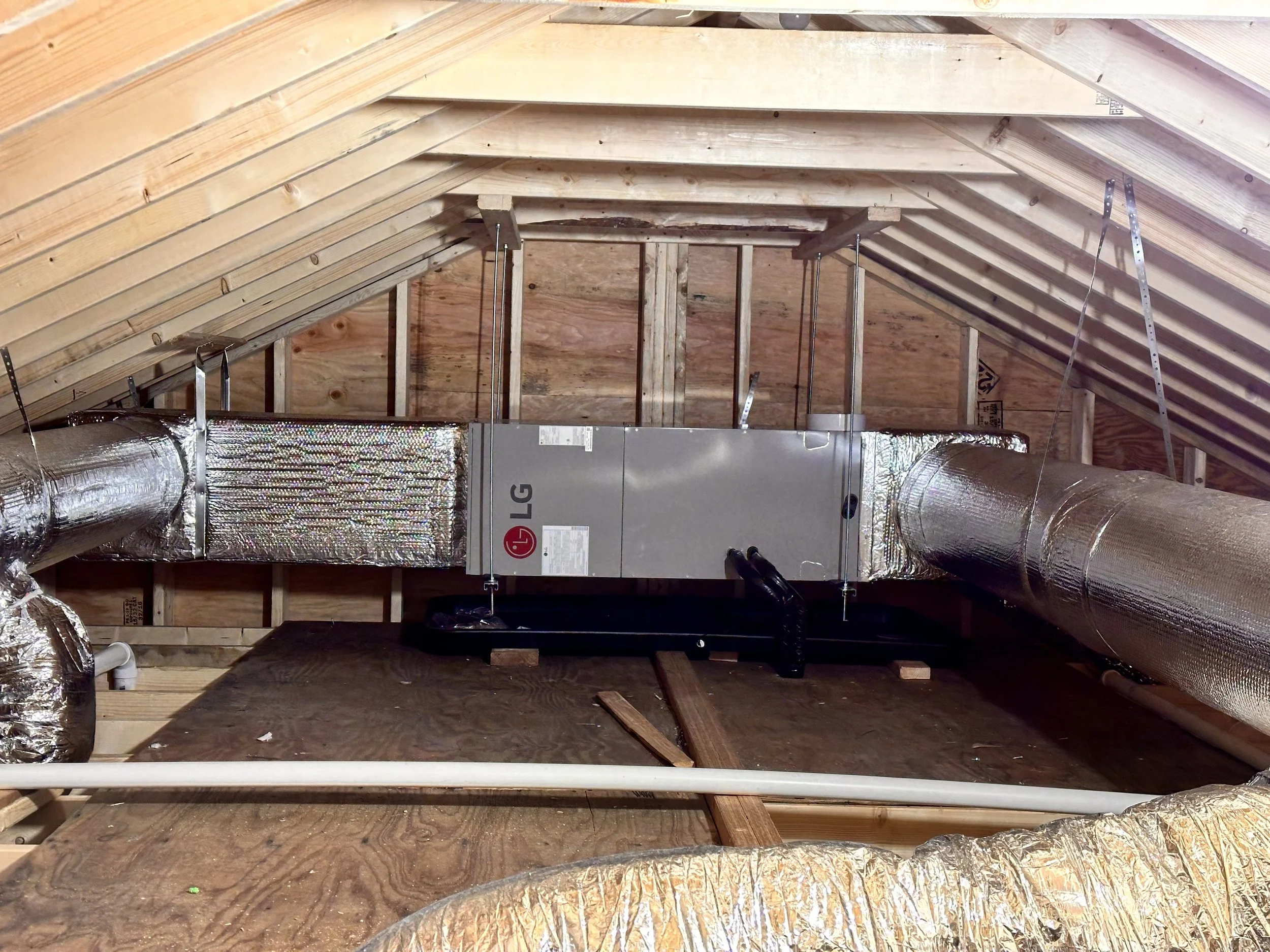 Attic with wooden roof trusses, HVAC ductwork, and metallic airflow pipes.