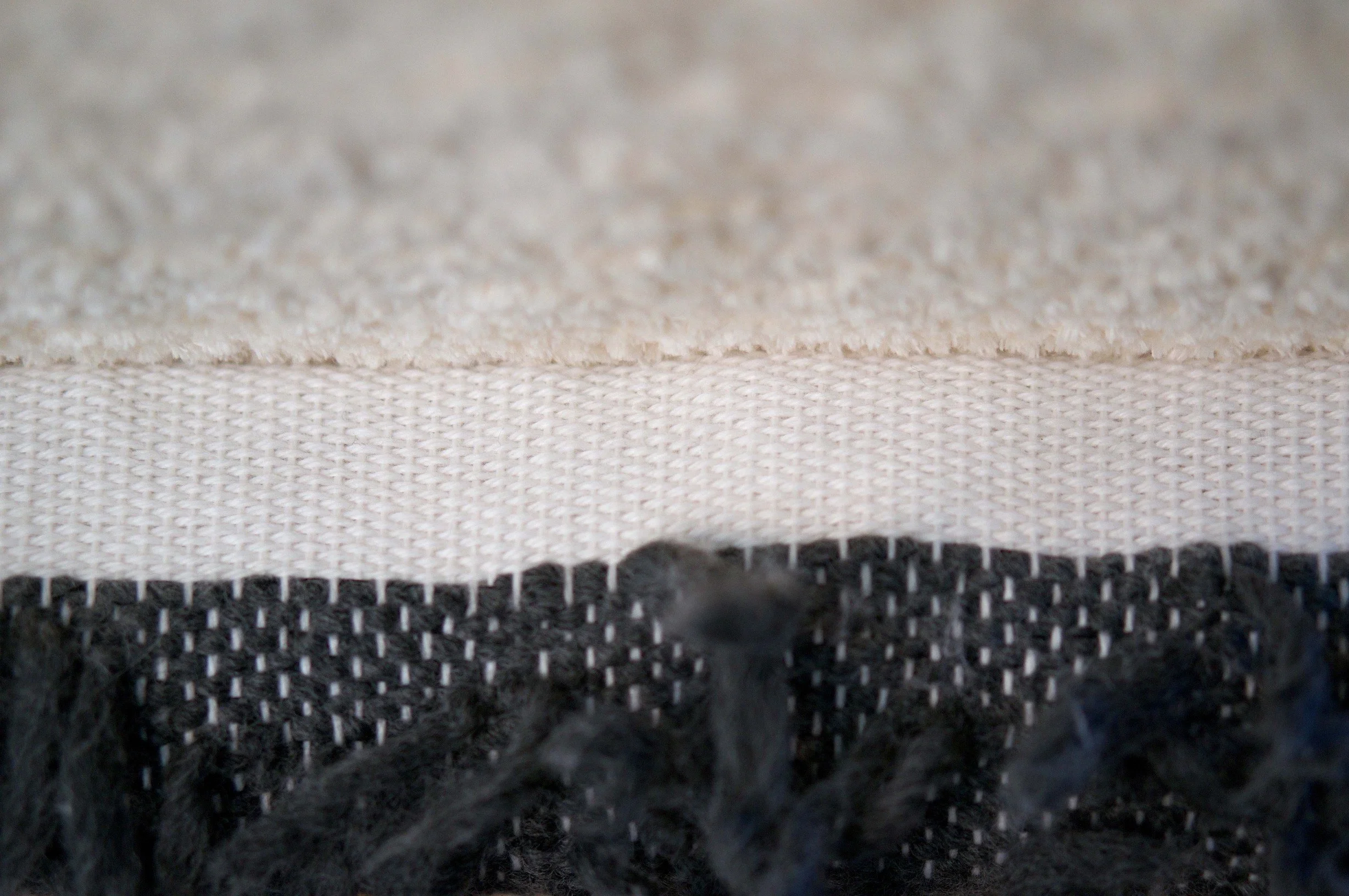 Macro view of layered woven textiles showing contrasting fibers and stitch structures, highlighting the tactile surface and craftsmanship of hand-woven fabric.