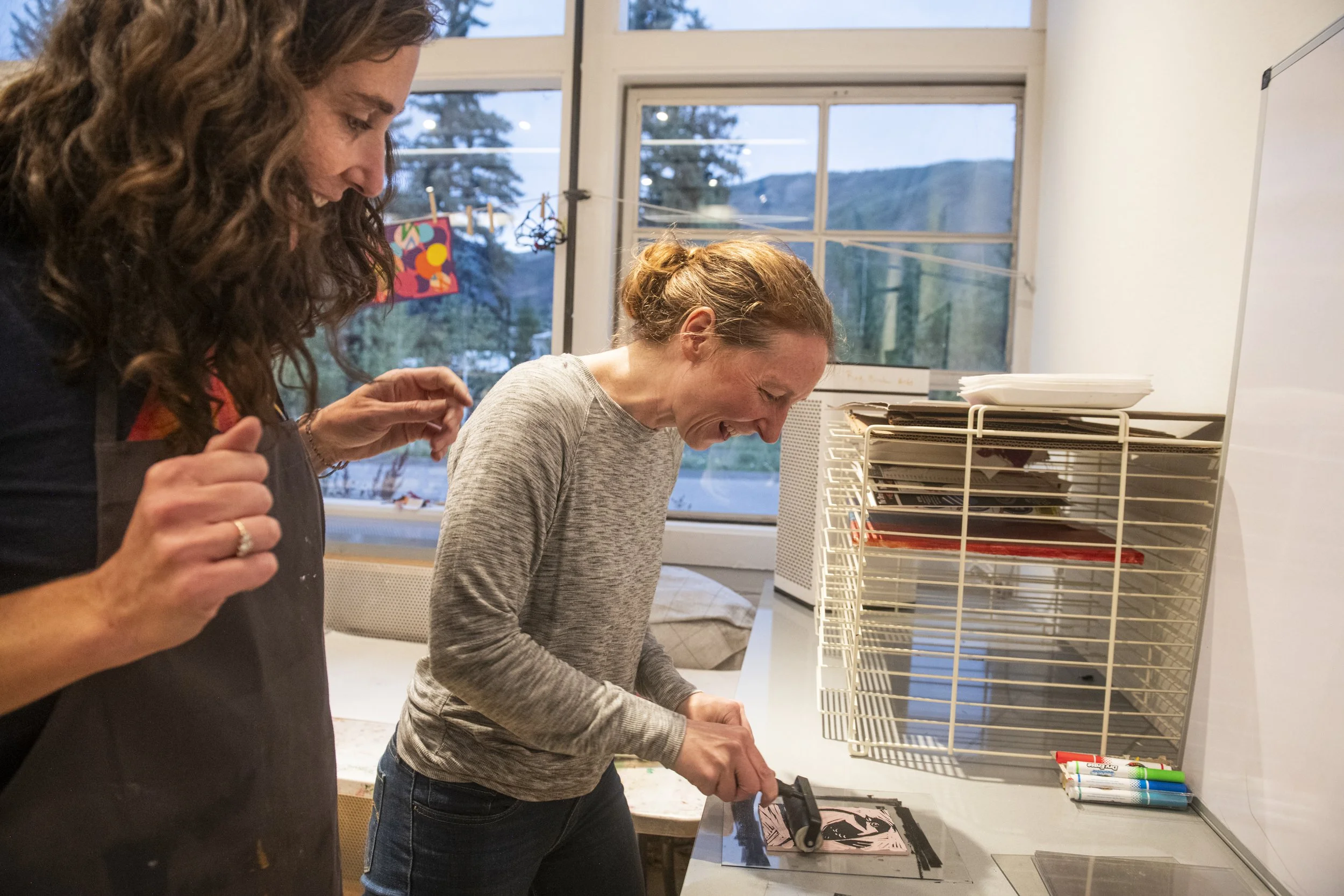 Woman rolling ink onto lino block with instructor watching