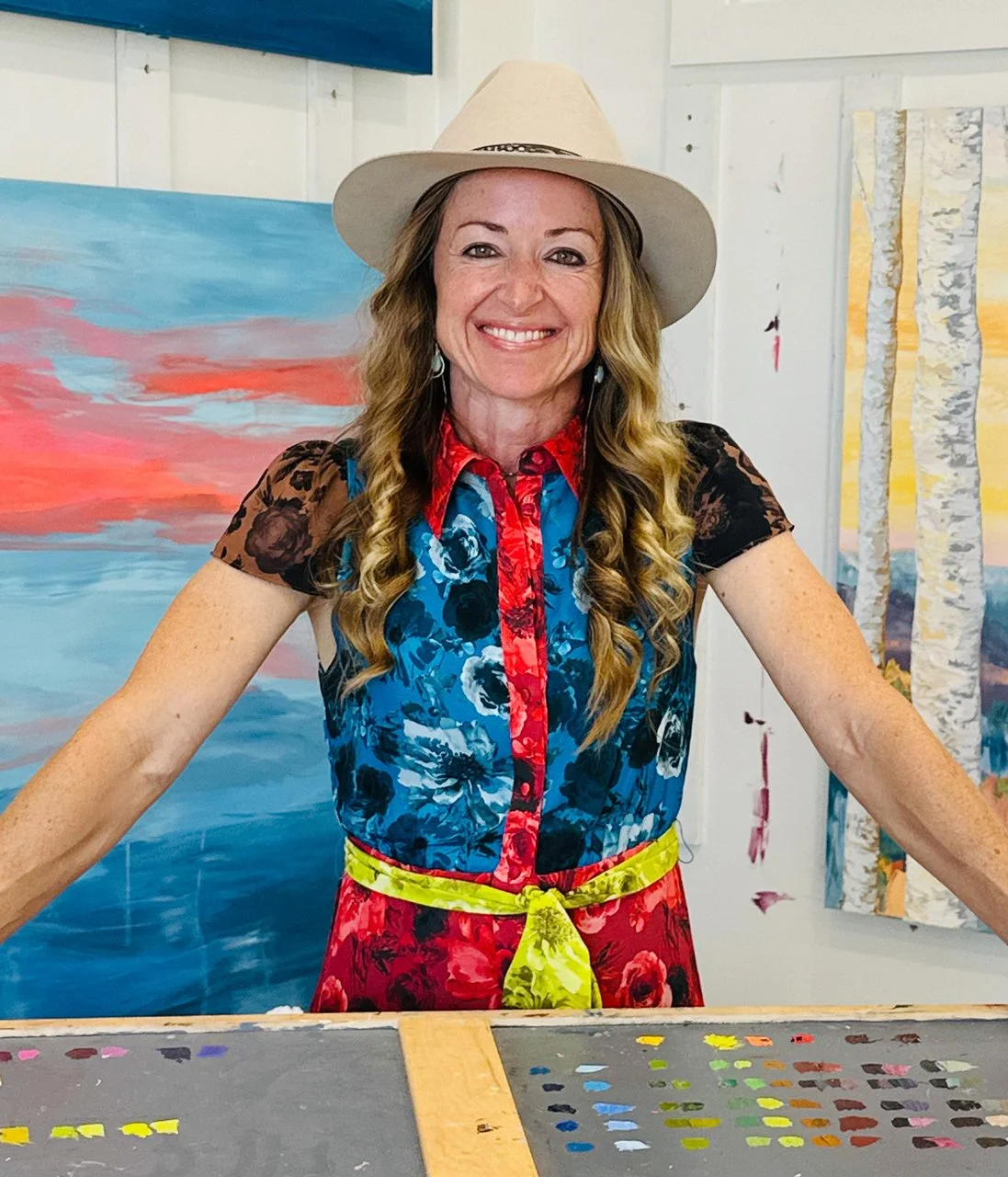 Artist Emily Chaplin stands in a colorful outfit in her studio near painting palettes