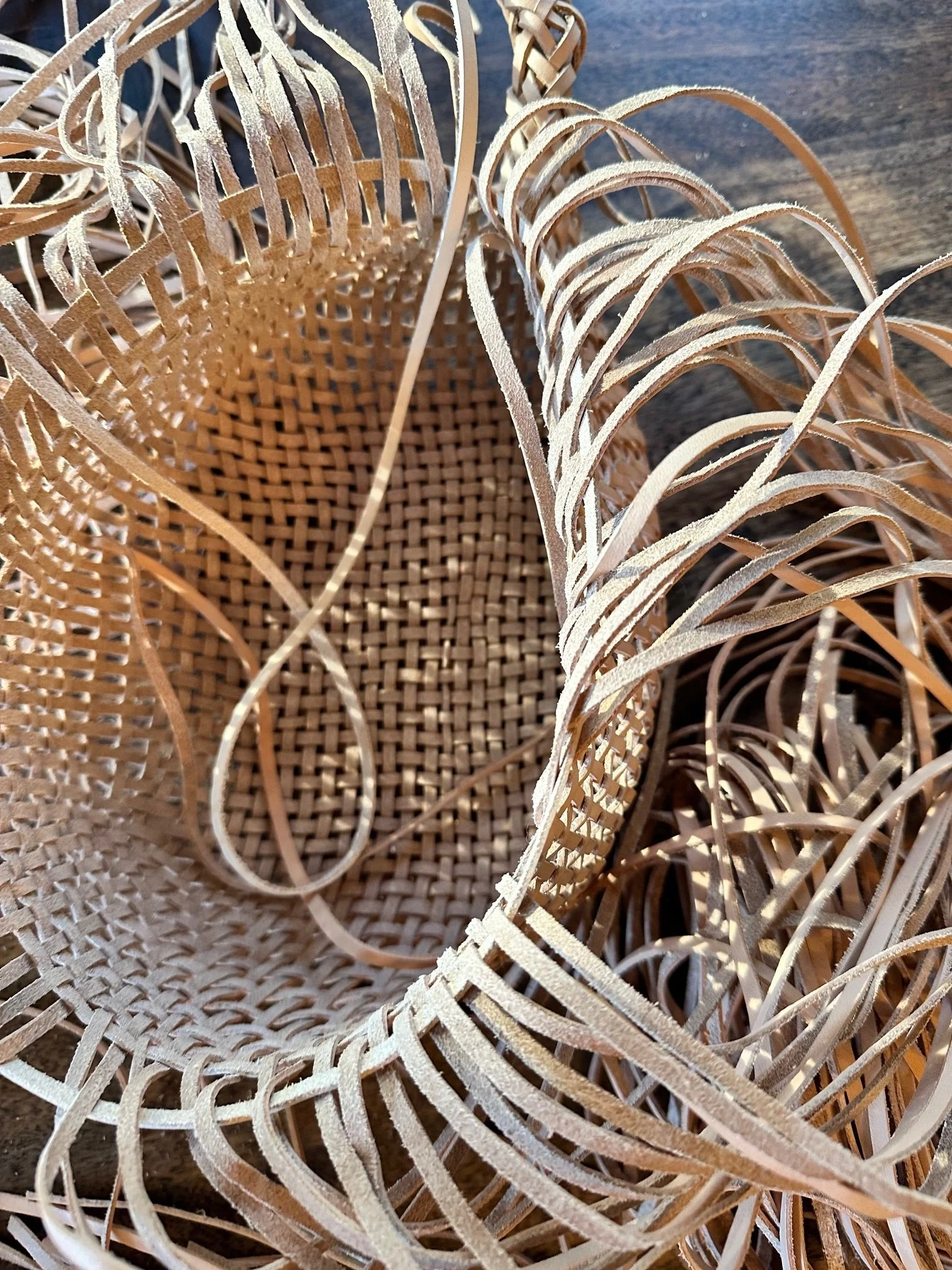 An in-progress weaving with long strips of natural leather being woven into a structured form.