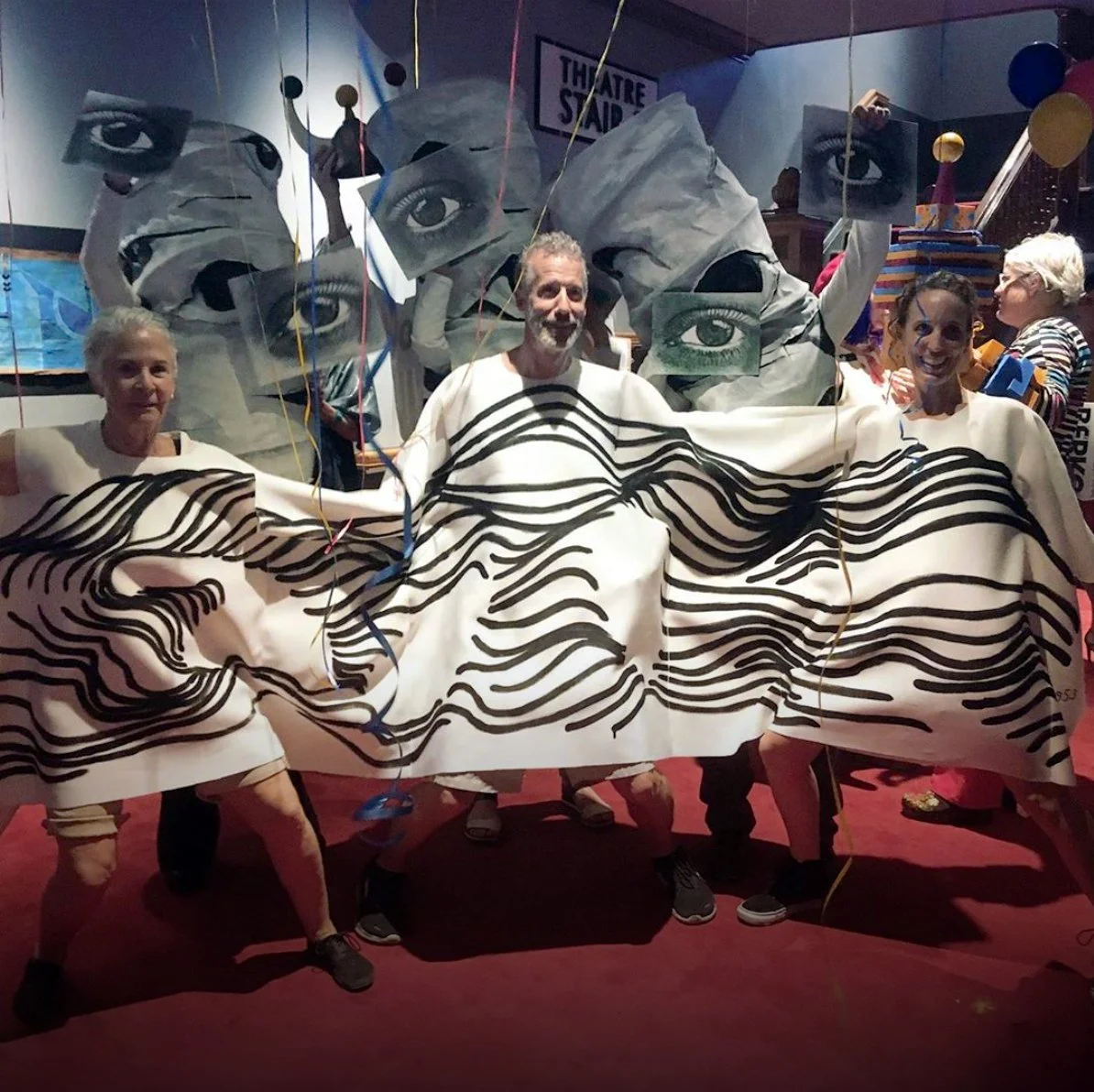 Three artists pose together in a combined Bauhaus-themed costume with wavy black lines on white tunics.