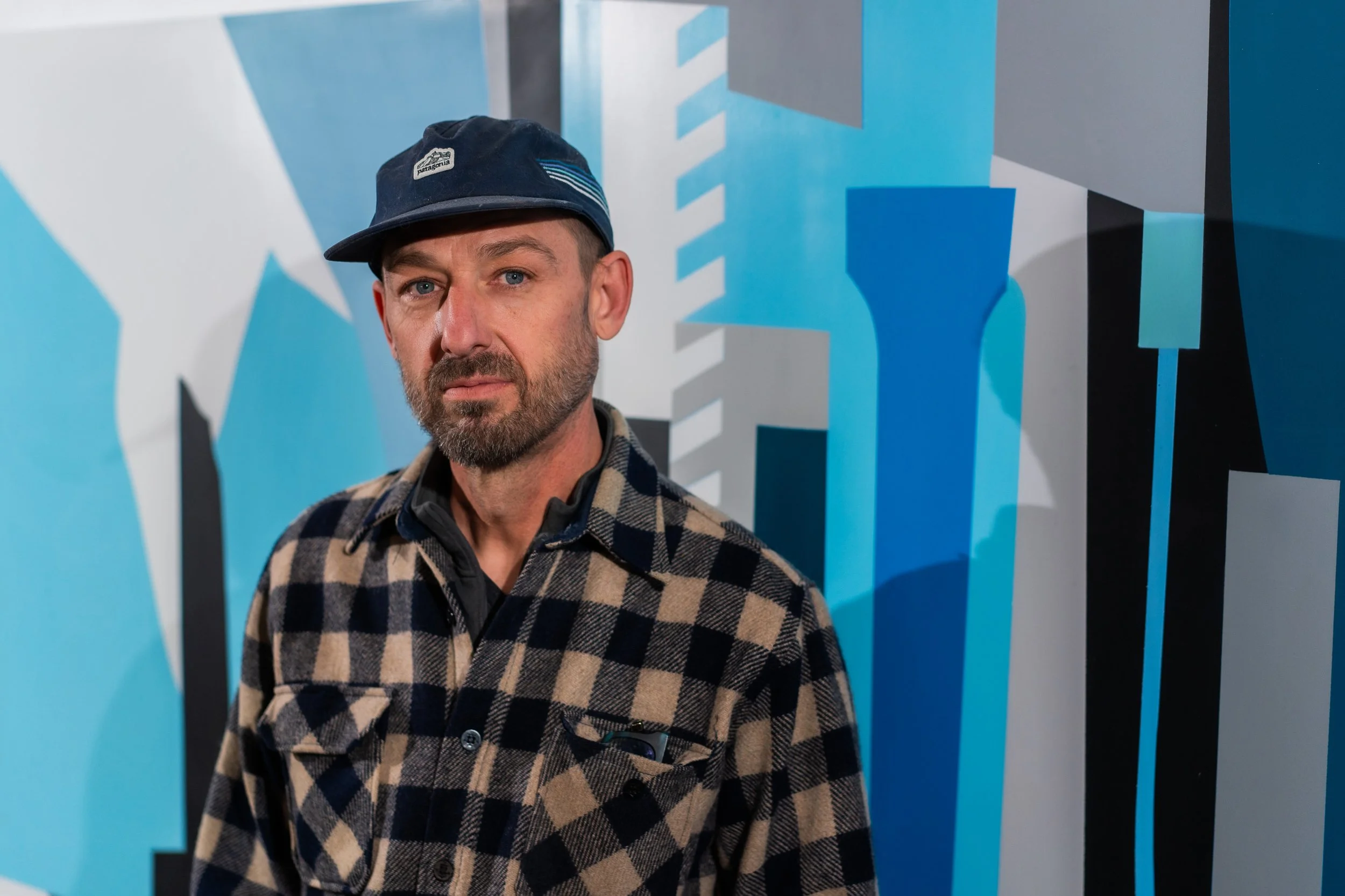 Artist Chris Erickson stands in front of some of his mural art with geometric blue and gray shapes