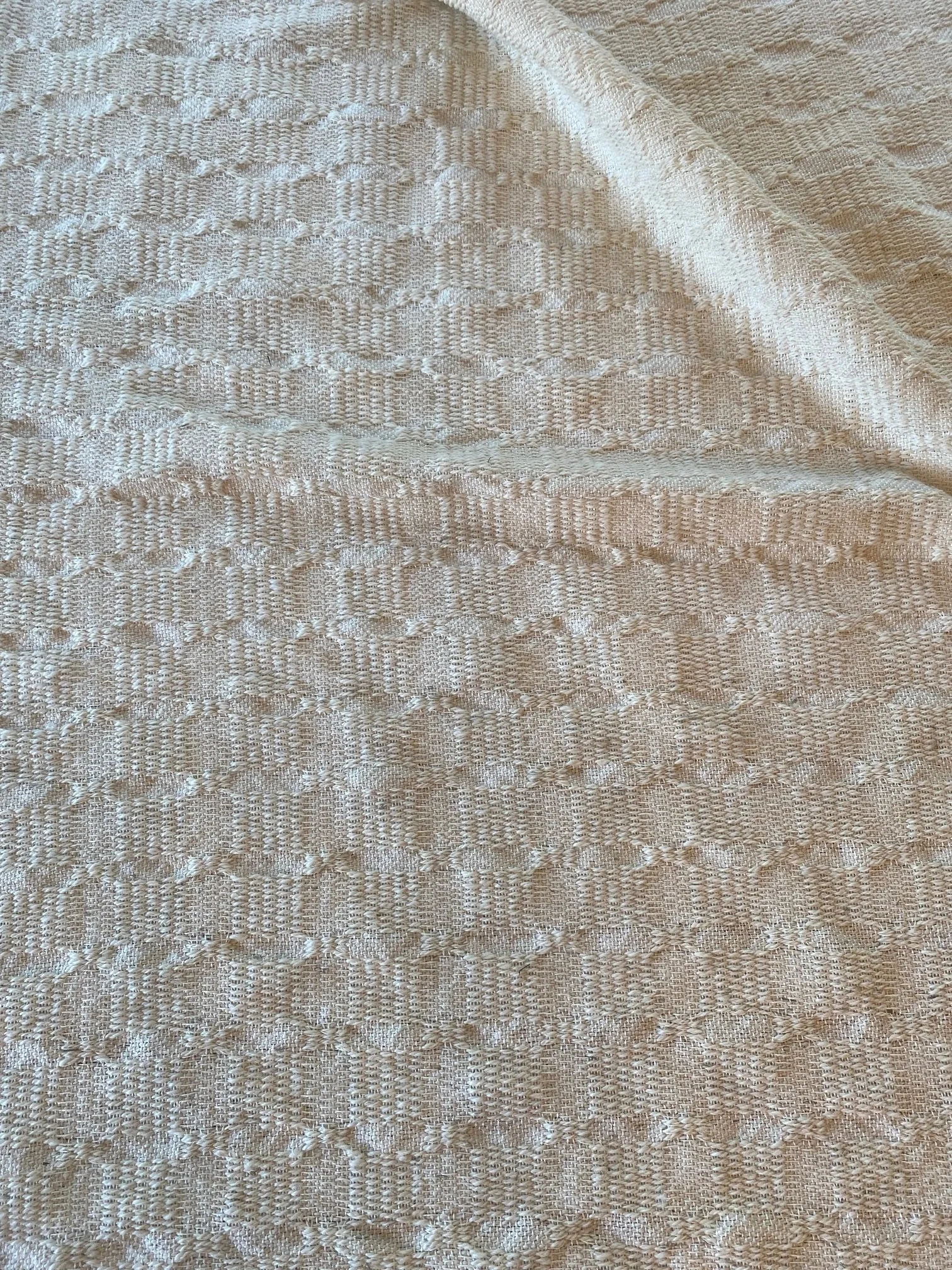 Soft cream woven textile with subtle raised geometric motifs, emphasizing the dimensional structure of the fabric.