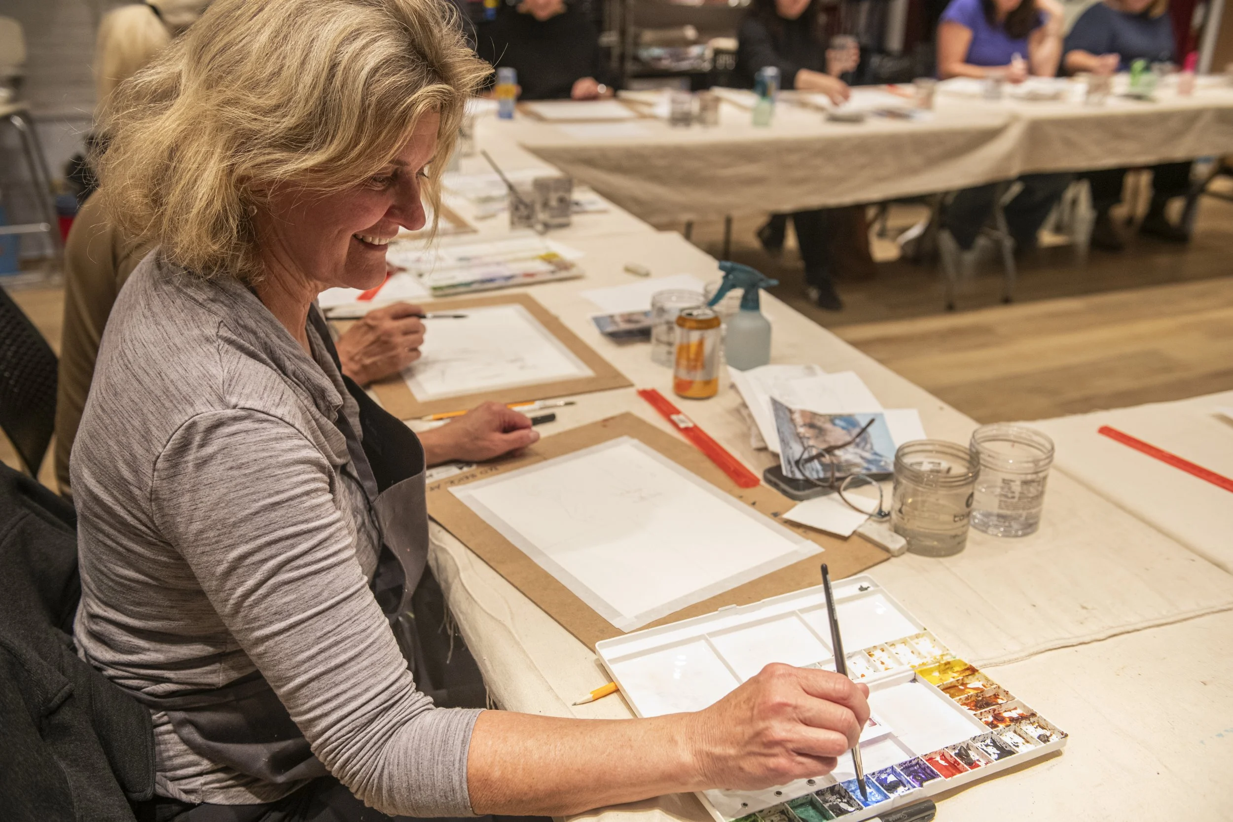 woman smiling as she dips her brush into watercolors