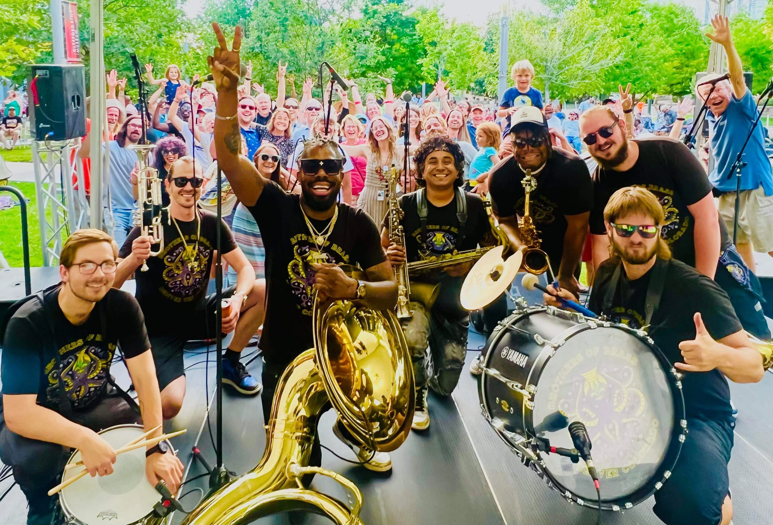 the Brothers of Bass band pose with their instruments in front of a crowd at an outdoor venue