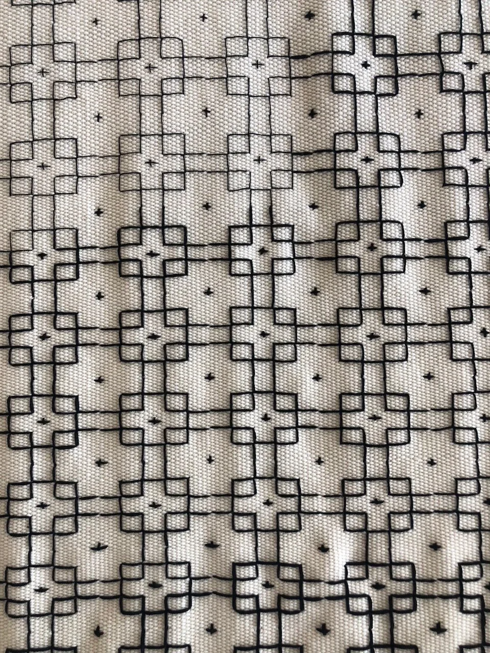 Hand-woven textile featuring a repeating geometric/rectagular pattern stitched in dark thread across a cream fabric ground.