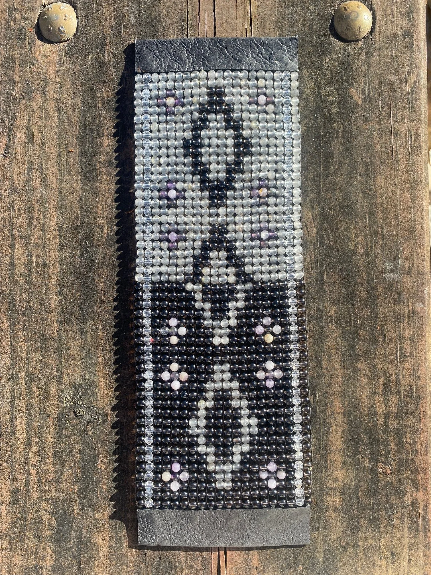 Bead-woven textile artwork using black, white, and translucent beads to create a symmetrical patterned panel.