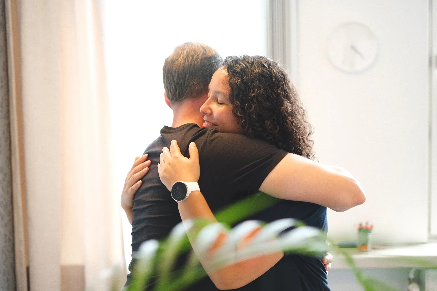 A man and woman hugging each other with eyes closed in a bright room.