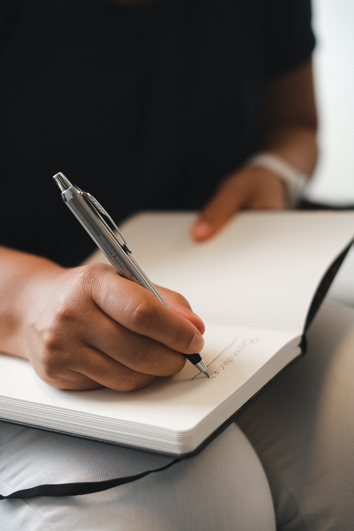 Person writing in a notebook with a silver pen.