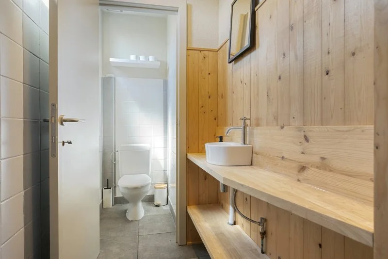 Een klein badkamer met een toilet en een houten wastafel met een ronde wasbak en een spiegel.