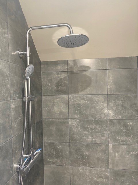 Douche met regendouchekop en handdouche tegen grijze betegelde muur.
