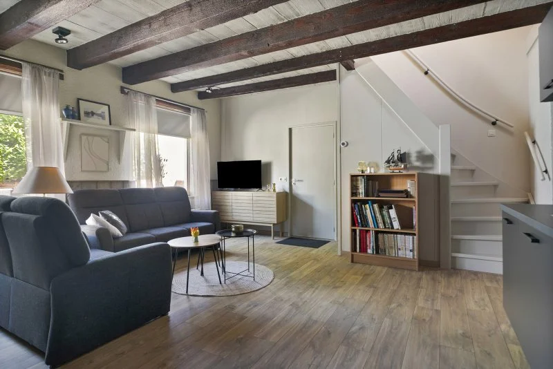 Woonkamer van het 4 persoon vakantiehuis te huur bij Paal, Kloosterzande met bank, salontafels, tv, boekenkast en trappen in een huis met houten plafonds en vloeren.