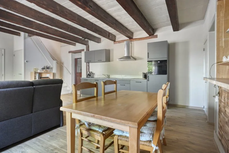 Open keuken en woonkamer in een huis met houten vloer en plafond met zichtbare houten balken.