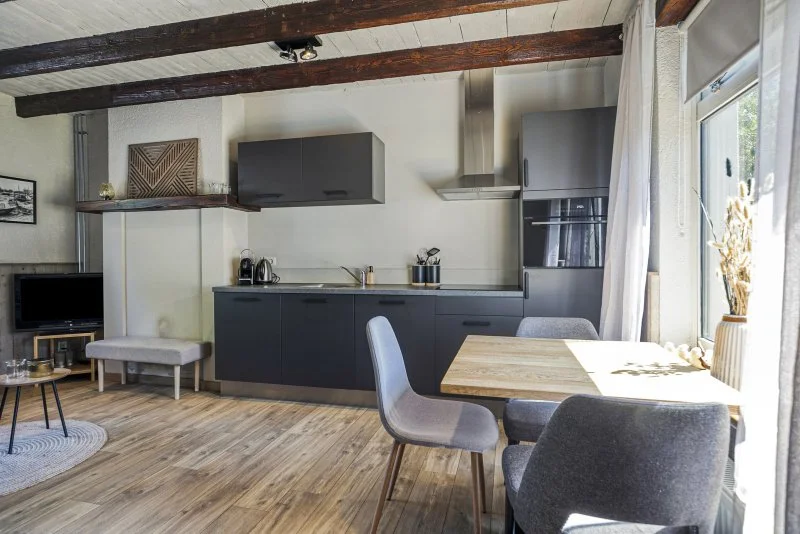 Moderne keuken en eettafel in een lichte woonkamer met grote ramen en houten vloer van het vakantiehuis 6 personen te huur in de regio van Hulst.