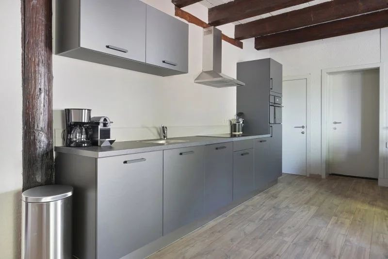 Moderne keuken met blauwe kasten, houten plafondbalken, en een koffiezetapparaat.