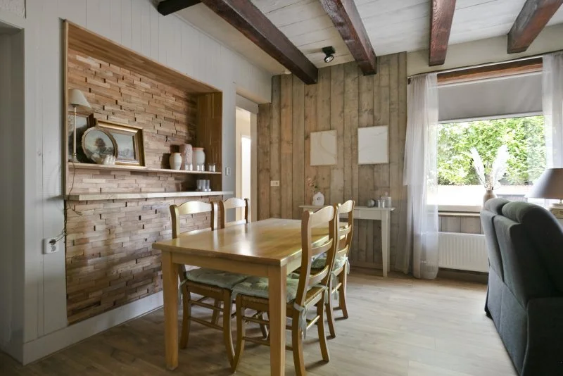 Eethoek in een woonkamer met houten tafel en stoelen, een raam met witte gordijnen, en muurdecoraties.