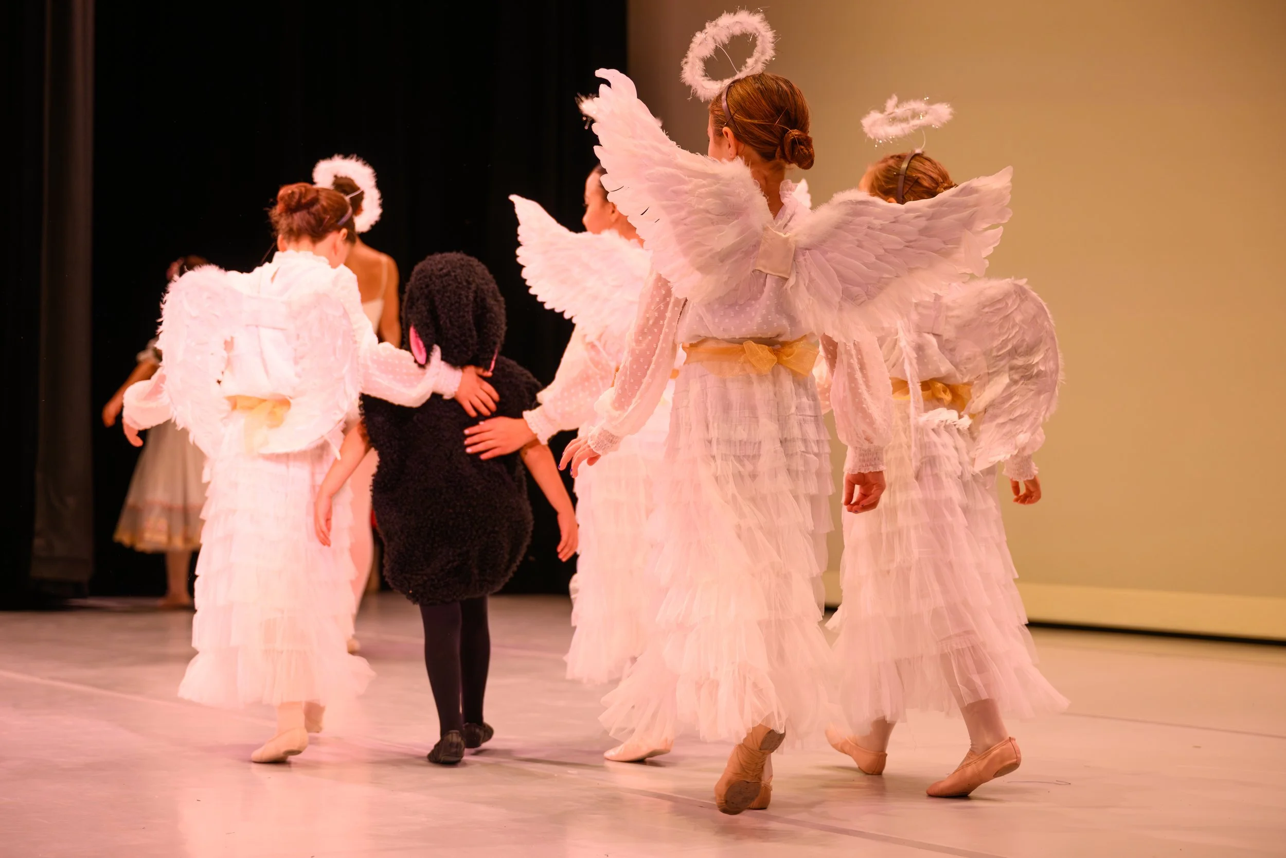 Children dressed as angels and a black sheep in a dance performance on stage.