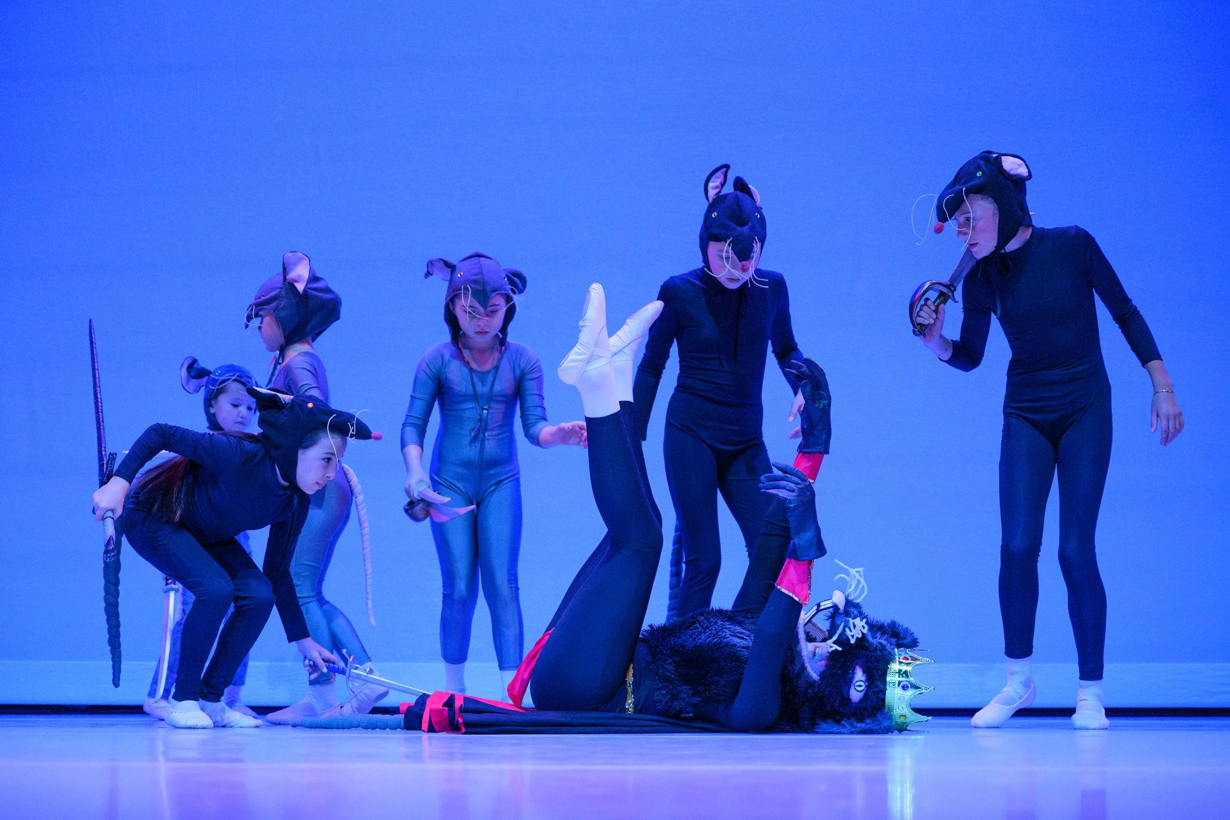 Children dressed in animal costumes, practicing a theatrical scene on stage with a blue background.