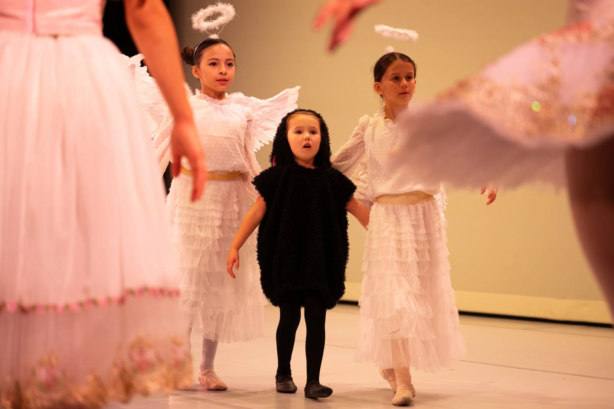 Young girls dressed as angels and a girl in a black sheep costume walking together during a stage performance