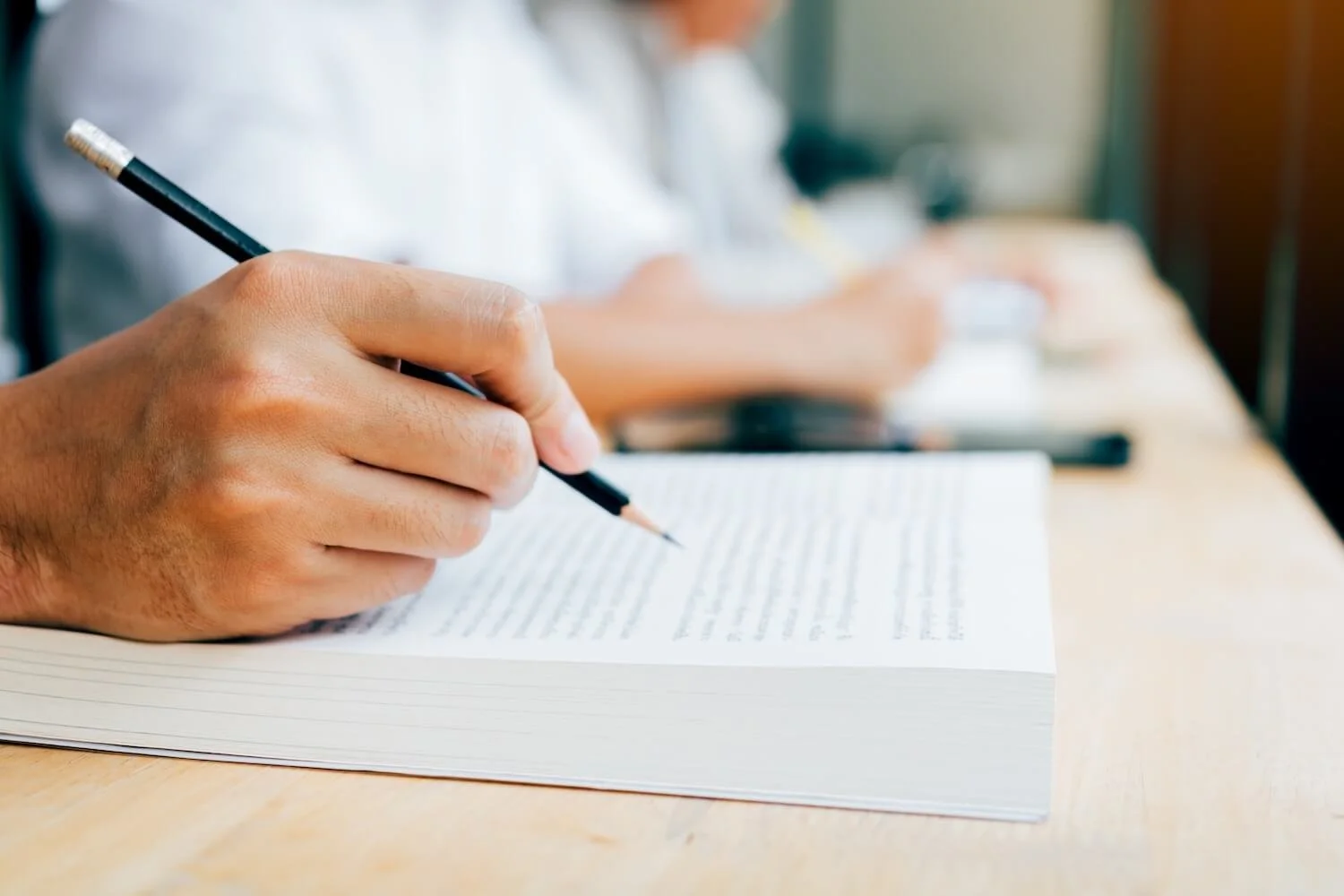 A student taking notes in a workbook during a quiet classroom study session