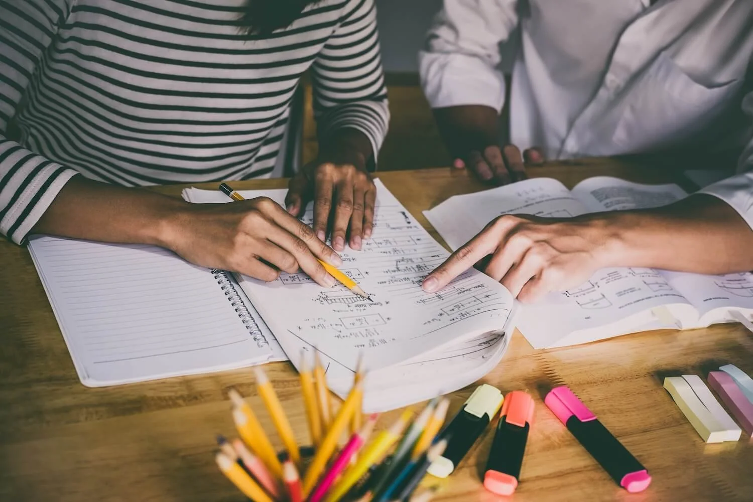 Close-up of two students working together on math problems with pencils and textbooks