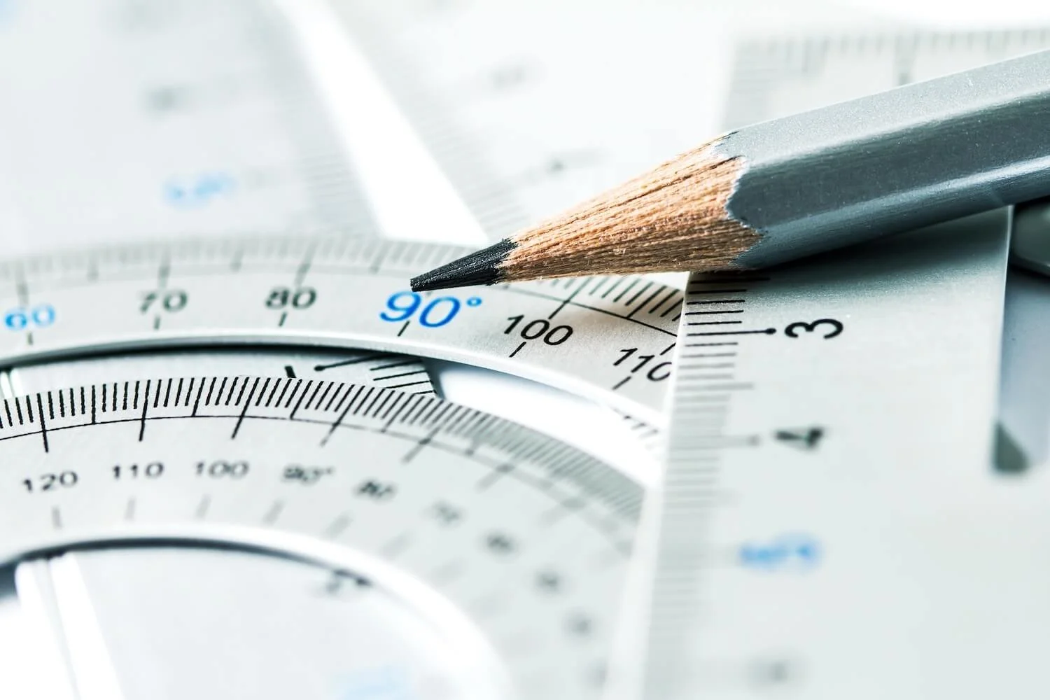Close-up of a pencil on top of overlapping protractors and geometry rulers