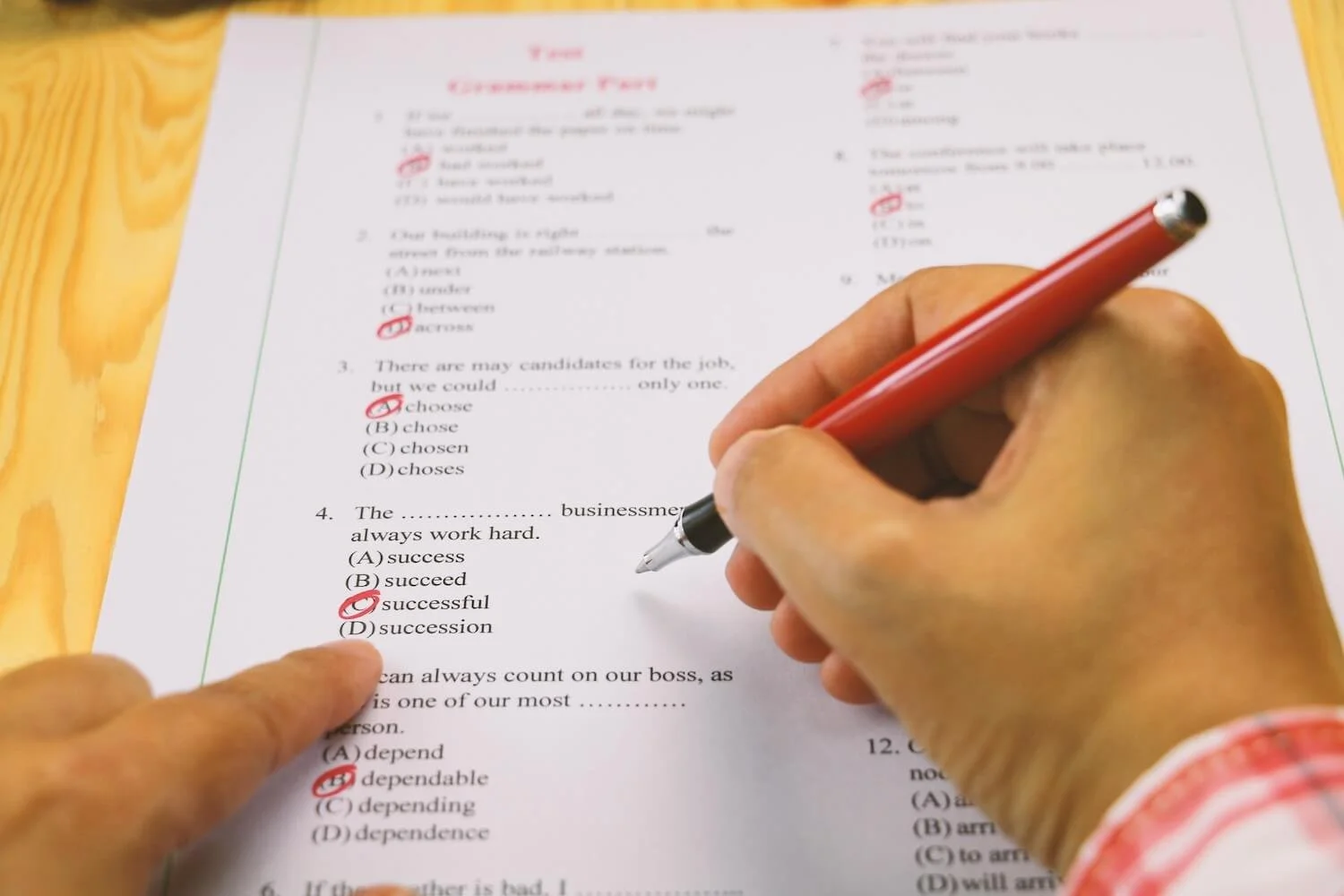 Person marking answers on a multiple-choice test or worksheet with a red pen, focusing on questions about choosing correct words.