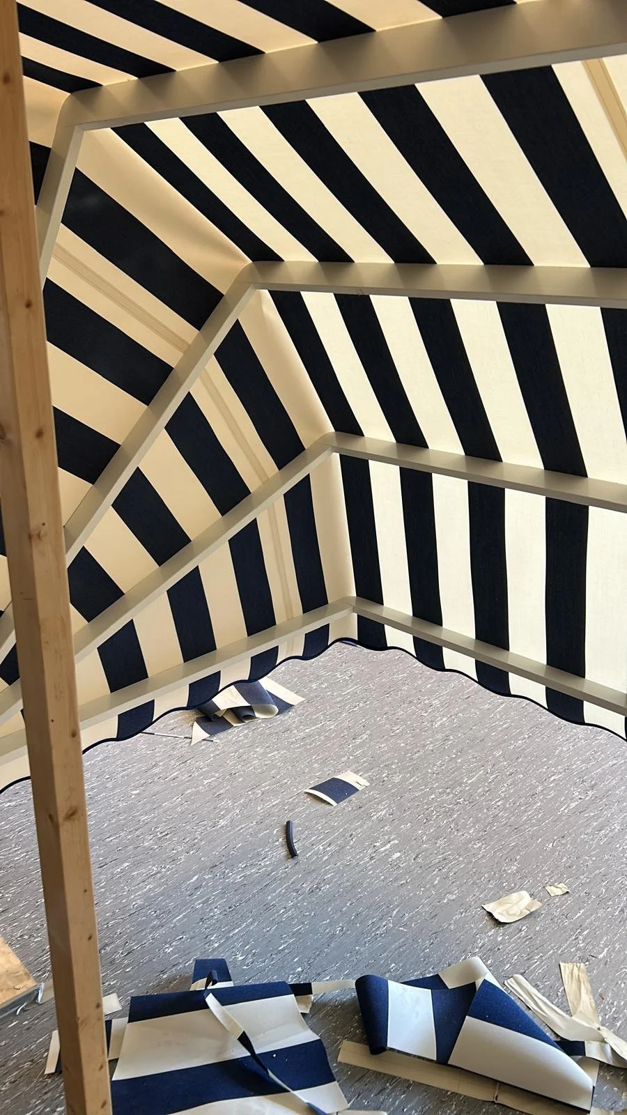 Binnenkant van een markies met zwart-witte gestreepte stoffen afwerking, met losse stukken stof en tape op de vloer.