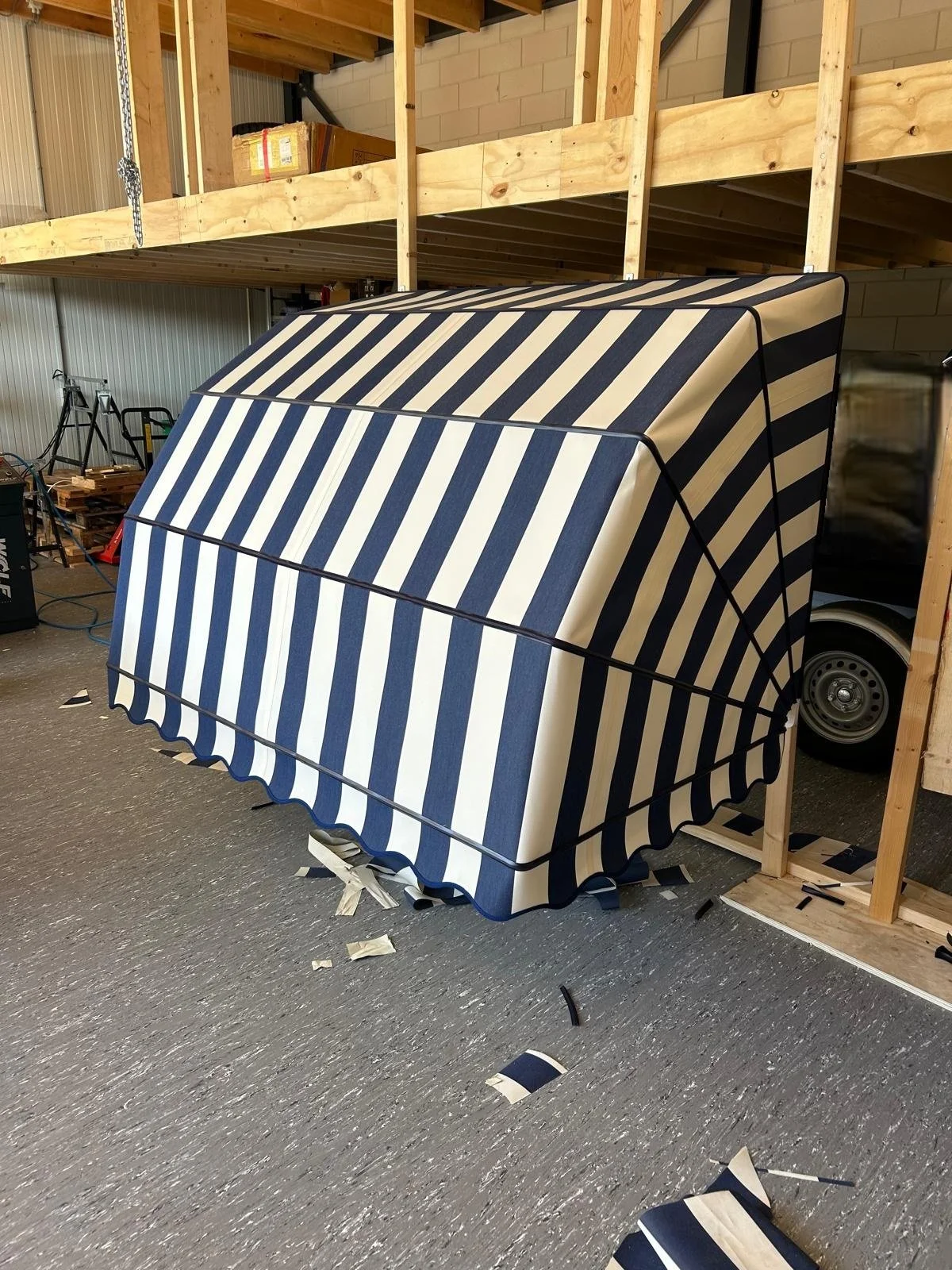 Een schuur met een tafel met een blauwe en witte gestreepte markies in het productieproces. Er liggen stukjes van het doek op de vloer.
