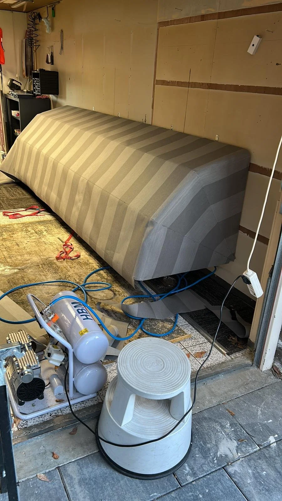 Een markies in productie, met een compressor en een krukje op de vloer, en een onvoltooide muur met houten latten.