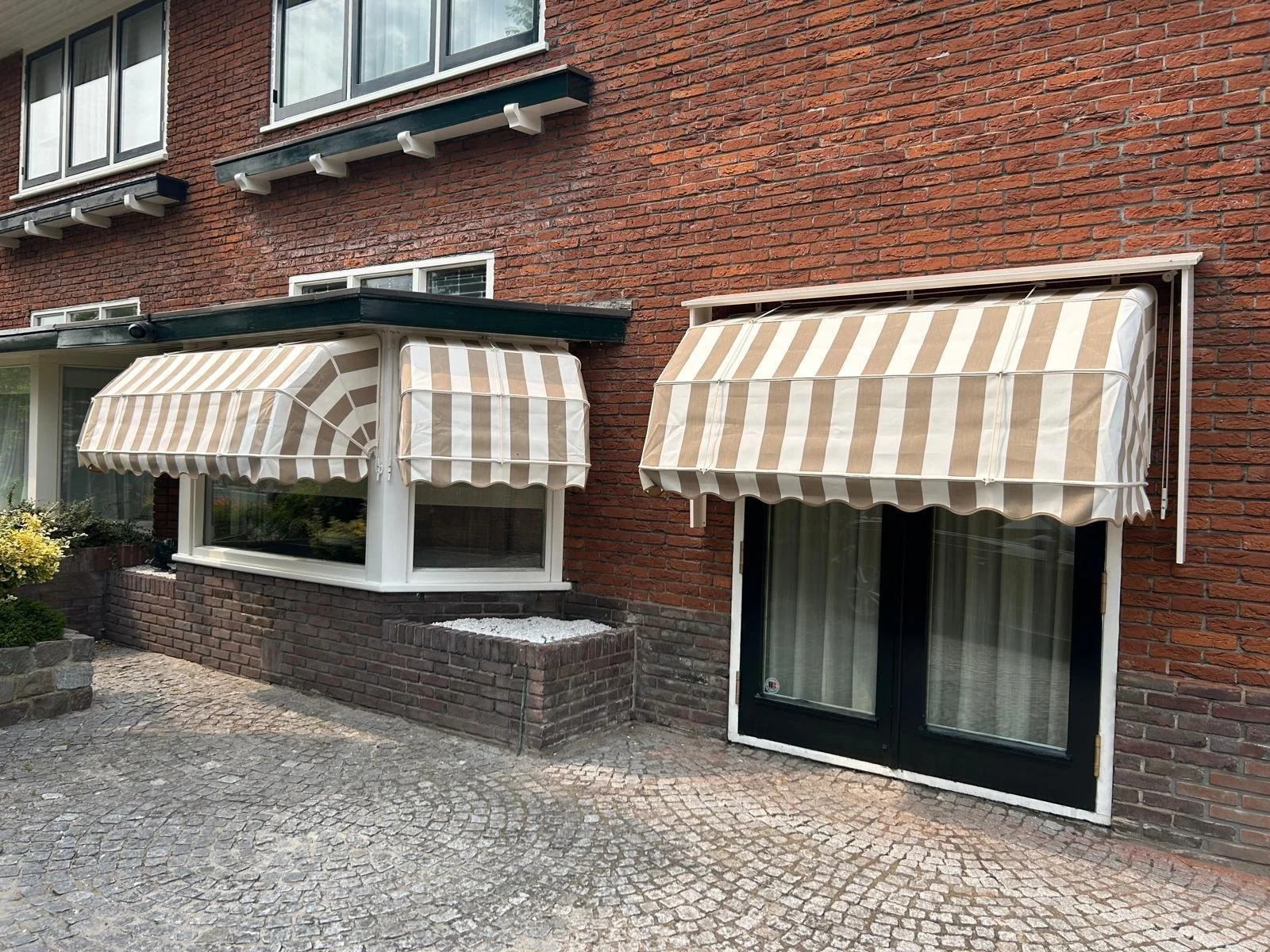 Buitenkant van een rood bakstenen appartement met twee met witte en beige gestreepte markiezen boven de ramen en een deur.