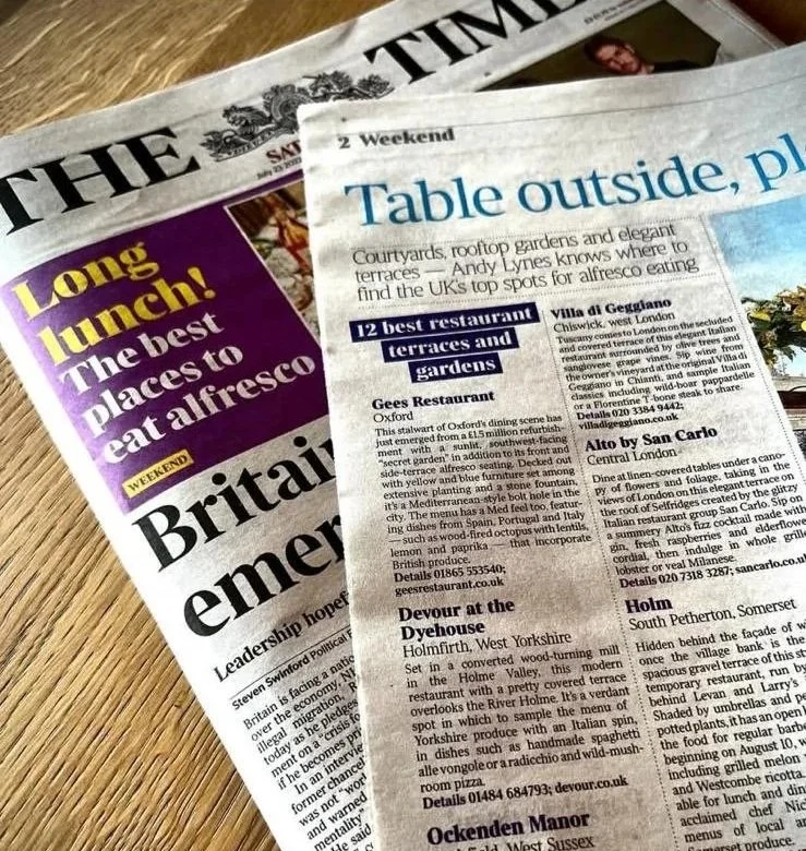 A copy of The Times newspaper opened to the 2022 article “Table Outside, Please,” featuring Devour at the Dyehouse, sat on a light wooden table — celebrating UK restaurant terraces and outdoor dining.