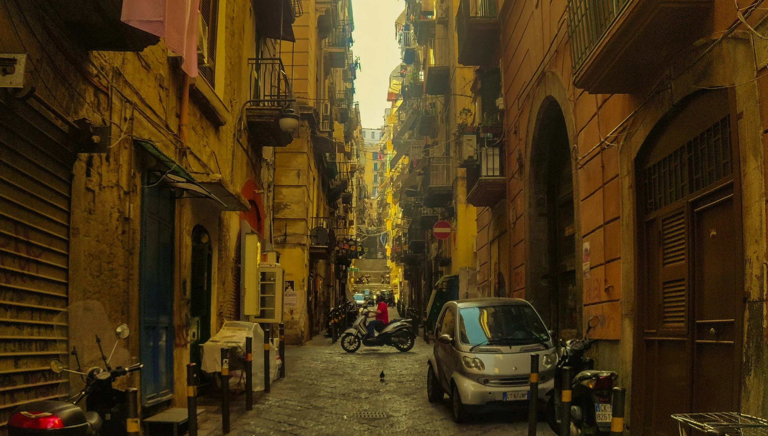 Historic narrow street in Naples filled with vendors, scooters and everyday life, capturing the energy and chaos of the city