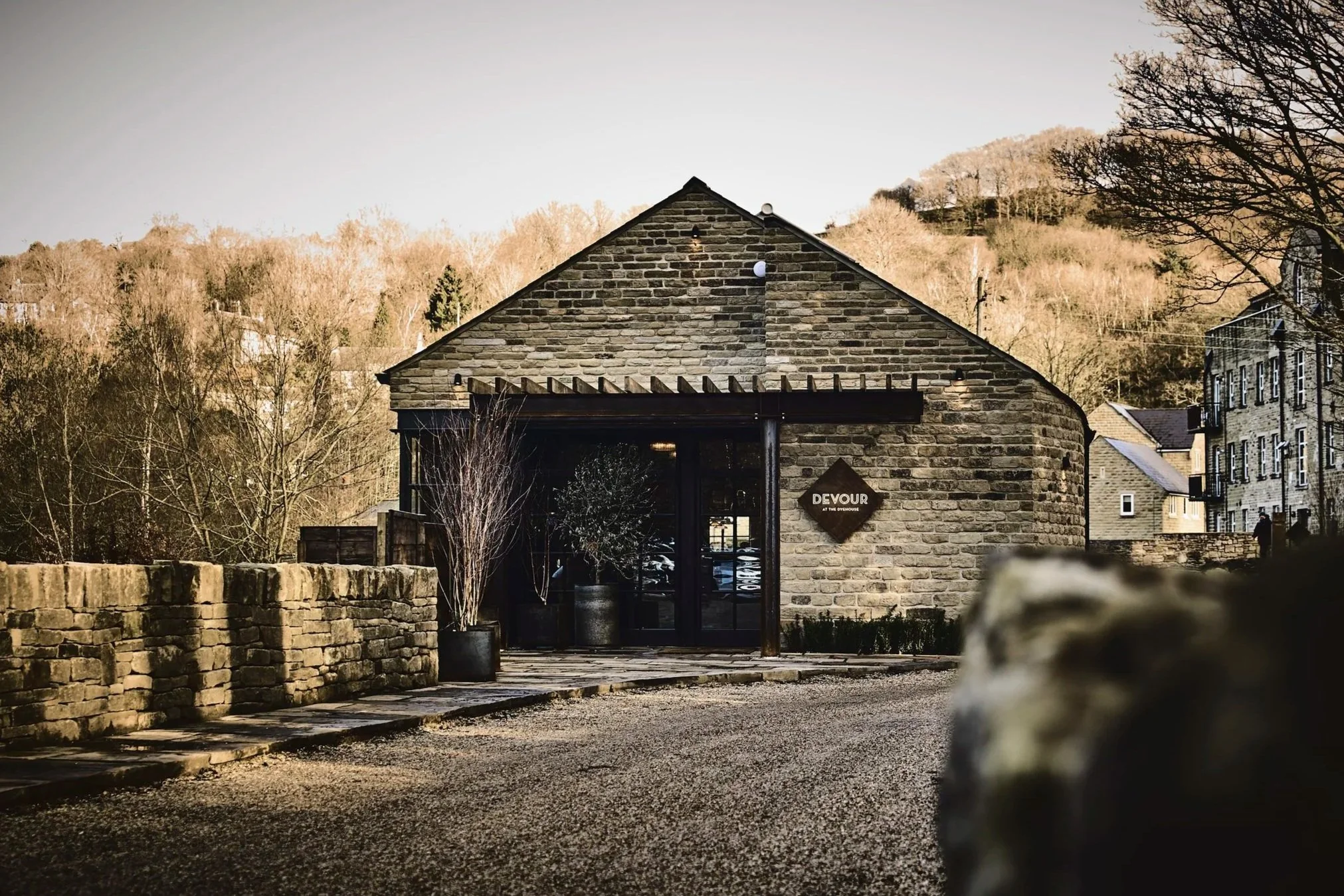Devour at the Dyehouse in Holmfirth, surrounded by trees and hills, with a gravel drive and traditional Yorkshire stone walls leading up to the restaurant.