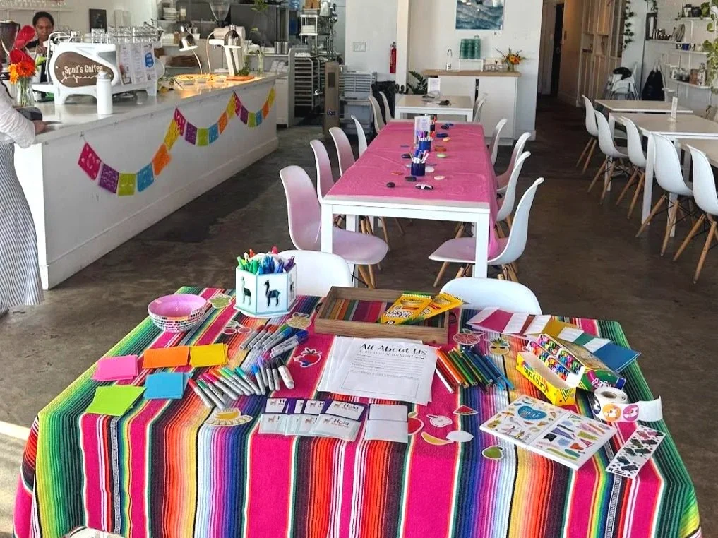 Decorative table with art supplies and craft materials for a party or event, set in a bright, modern space with pink, white, and colorful decor.