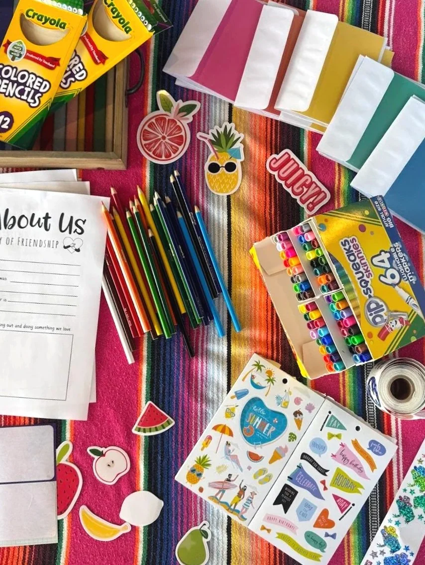A colorful table with art supplies, including Crayola colored pencils, markers, and stickers, on a bright, striped tablecloth.