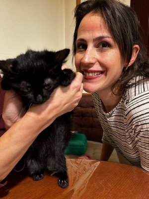 Una mujer sonriendo con una niña que sostiene un gato negro en brazos.