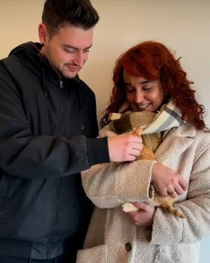 Un hombre y una mujer sonriendo, con la mujer sosteniendo una pequeña pila de dinero.