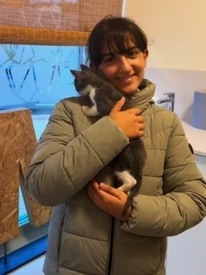 Una joven sosteniendo un gatito gris y blanco en un ambiente interior