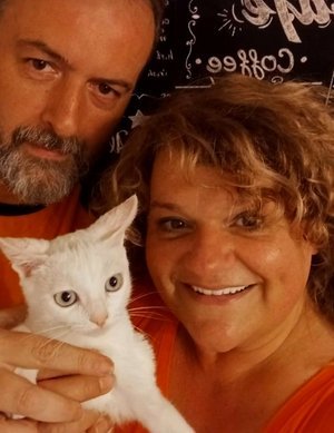 Dos personas sonriendo junto a un gato blanco.
