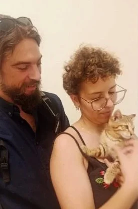 Una mujer sostiene un gato anaranjado mientras un hombre observa.